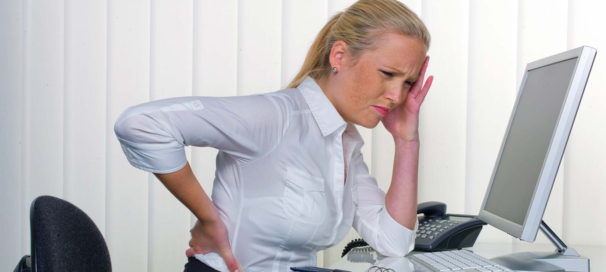 Office worker experiencing a headache, neck and back pain at a computer.